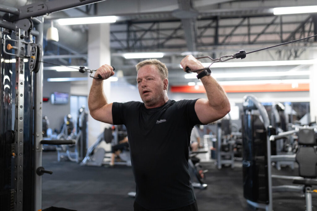 A mature yet fit client performing a strength exercise on a cable machine at Virgin Active The Sanctuary in Somerset West, showcasing his dedication to maintaining excellent health and vitality.