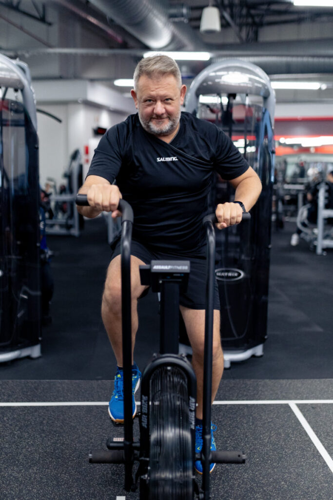 A mature client engaging in a vigorous cardio workout on an air bike at Virgin Active The Sanctuary in Somerset West, demonstrating commitment to heart health and fitness at any age.