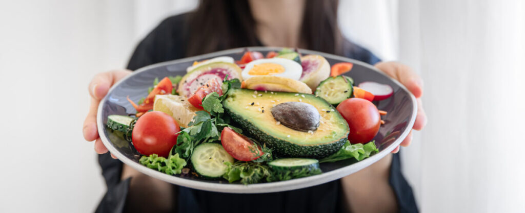 A person holding a vibrant, heart-healthy poke bowl featuring avocado, tomatoes, cucumbers, eggs, and leafy greens, similar to the nutritious options available at Kauai within Virgin Active The Sanctuary in Somerset West, emphasizing the vital role of a nutrient-rich diet in supporting overall health.