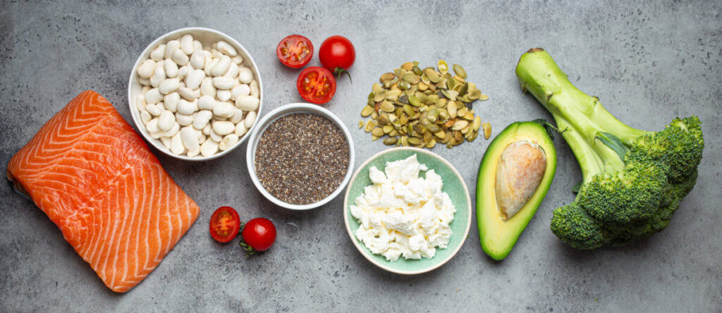 A vibrant display of heart-healthy ingredients including salmon, white beans, chia seeds, cottage cheese, avocado, broccoli, cherry tomatoes, and pumpkin seeds, illustrating the benefits of good fats over bad fats, as recommended for optimal cardiovascular health at Virgin Active The Sanctuary in Somerset West